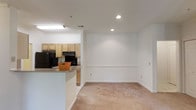 This single-floor residence offers three bedrooms and two bathrooms within a well-proportioned floor plan designed for comfortable living. The open-concept layout connects the kitchen and living area seamlessly, creating a bright and functional shared space. The kitchen features light wood cabinetry, black appliances including a refrigerator and range, and a breakfast bar peninsula with a granite-style countertop that provides additional prep space and casual dining options. Recessed lighting and a fluorescent fixture illuminate the kitchen, while recessed ceiling lights extend into the living area, enhancing the airy feel of the space. The living area is finished with neutral wall-to-wall carpeting and crisp white walls accented by a chair-rail molding detail, contributing to a clean and classic aesthetic. The white trim and baseboards throughout add a polished, cohesive look. The open sightlines between the kitchen and living room make the space feel expansive and inviting, ideal for both everyday living and entertaining. With three bedrooms, the layout offers flexibility for various living arrangements, providing ample private space alongside the generous shared areas.