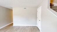 Located at 1671 Fort Campbell Blvd in Clarksville, TN, this two-story unit offers a practical and well-organized layout split evenly across two floors. The main level features a combined kitchen and living area with light wood-look flooring throughout. The kitchen is outfitted with white shaker-style cabinetry, white subway tile backsplash, light countertops, a stainless steel refrigerator, stainless range with over-the-range microwave, and a single-basin sink. A louvered closet door provides additional storage. Natural light enters through a windowed exterior door, giving the kitchen a bright, airy feel. The adjoining living room is open and neutral-toned with a textured ceiling and easy access to the staircase. Upstairs, both bedrooms feature plush carpet, neutral wall tones, and ceiling fans with light fixtures. Each room benefits from natural light through windows with outdoor views of surrounding greenery. The primary bedroom includes a closet. A full bathroom on the upper level offers a tub/shower combo with white tile surround, a vanity with marble-style countertop, and wood-look flooring that ties the space together cohesively.