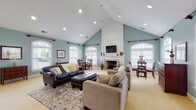 Located at 3900 Suffolk Dr in Dublin, Ohio, this single-floor space impresses with its open, airy layout and thoughtful architectural design. The centerpiece of the main living area is a dramatic vaulted ceiling that rises to a striking peak, accentuated by a ceiling fan and recessed lighting that illuminate the space throughout. Soft sage-blue walls create a calming, cohesive palette that flows through every room.

A grand fireplace with a white-painted surround, brick hearth, and an elevated white mantel serves as a true focal point of the living room. Arched windows with plantation shutters line the walls, flooding the interior with natural light and offering views of the surrounding neighborhood. The generous living area comfortably accommodates multiple seating arrangements, with plush carpeting adding warmth underfoot.

Adjacent to the living room, a cozy dining nook features a glass-top round table nestled beneath arched windows, providing an intimate setting bathed in natural light. The kitchen is efficiently designed with white cabinetry, dark countertops, tile flooring, a double sink, and ample counter space — practical and clean in its layout. A breakfast bar provides additional seating.

Throughout, the space maintains a warm, welcoming ambiance with consistent finishes, generous proportions, and an abundance of natural light.