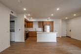 Located at 9174 Indiana Ave in Riverside, California, this single-story unit presents a contemporary design with a clean, neutral palette and modern finishes throughout. The open-concept layout connects the living area and kitchen seamlessly, creating a bright and functional space enhanced by recessed lighting and a ceiling fan overhead.

The kitchen is a standout feature, showcasing warm wood-tone flat-front cabinetry, white quartz countertops, and a classic white subway tile backsplash. A central island provides additional prep and seating space, while a full suite of stainless steel appliances—including a gas range, built-in microwave, dishwasher, and refrigerator—completes the space. Light hardwood-style flooring runs throughout the main living areas, adding warmth and continuity.

The bedrooms offer a comfortable retreat, finished with plush neutral carpeting and windows fitted with horizontal blinds that allow for natural light and privacy. One bedroom features hardwood-style flooring and a ceiling fan. The bathroom is appointed with a dual-sink vanity, wood-tone cabinetry, white quartz countertops, a large mirror, and a tub-shower combination with white tile surround, maintaining the cohesive modern aesthetic found throughout the unit.