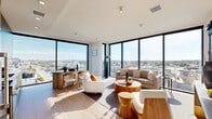 This thoughtfully designed one-bedroom, one-bathroom residence offers a refined modern aesthetic with high-end finishes throughout its generously proportioned single-floor layout. The standout feature is the living area, where floor-to-ceiling corner windows flood the space with natural light and frame expansive panoramic city views, creating a bright, airy atmosphere that defines the entire unit.

The open-plan kitchen and living room are seamlessly connected, making the space ideal for both daily living and entertaining. The kitchen is outfitted with sleek, steel-toned flat-front cabinetry extending from floor to ceiling, dark countertops, a stainless steel range, and a matte black faucet — all complemented by large windows that continue the city views into the cooking space. A compact dining area with a rounded table sits adjacent to the kitchen.

The bedroom is a calm, well-proportioned retreat featuring light wood flooring, a textured built-in wardrobe with a linear grain finish, and access to the bathroom. The bathroom maintains the unit's clean aesthetic with terrazzo-style flooring, a navy-framed mirror, and crisp white walls. Light wood flooring and recessed lighting run consistently throughout, unifying the space with a cohesive, contemporary character.
