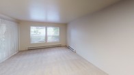 Located in the Lake City neighborhood of Seattle, WA, Unit 219 at 13725 32nd Ave NE is a single-floor residence designed with a clean, functional layout. The living and sleeping areas feature neutral-toned wall-to-wall carpeting, creating a warm and comfortable atmosphere. Each room is equipped with baseboard heating and vertical blind window treatments, with windows allowing natural light to filter in and offering views of the surrounding neighborhood. Ceiling-mounted flush lights provide additional illumination throughout.

The galley-style kitchen is a standout feature, finished with rich dark cabinetry contrasted against light wood-look flooring. It includes a full suite of appliances — an electric range, stainless steel refrigerator, and built-in dishwasher — along with dark countertops and a stainless steel sink. Overhead, a recessed skylight panel brightens the kitchen workspace efficiently.

The bathroom is accessible via a dark-framed door and features wood-look flooring, a dark vanity cabinet, and clean, functional fixtures. An adjacent closet area provides convenient built-in shelving for storage. The overall aesthetic of the unit is neutral and move-in ready, with consistent finishes that create a cohesive, understated living environment throughout.
