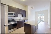 Located at 100 Rosie Square in Wood-Ridge, NJ, this one-bedroom, one-bathroom residence offers a well-designed single-floor layout that maximizes functionality and comfort. Light-toned hardwood-style flooring runs throughout, complementing the bright, neutral palette found in every room.

The open-concept kitchen and living area serves as the heart of the home. The kitchen is outfitted with dark espresso cabinetry, a classic white subway tile backsplash, a stainless steel appliance suite including a gas range, microwave, dishwasher, and refrigerator, and a central island with a light quartz countertop that provides additional prep and seating space. The living area flows naturally from the kitchen and is bathed in natural light from a large sliding glass door that opens to an outdoor view.

The bedroom is a generously sized, quiet retreat with large windows that allow ample natural light and outdoor views of the surrounding neighborhood. Two closets, including a spacious walk-in closet with multi-tier wire shelving, offer excellent storage capacity.

The bathroom features a clean, modern design with a white vanity, a well-lit mirror, and a tub-shower combination. Additional conveniences include a dedicated laundry area and a utility room, rounding out this efficiently designed and move-in-ready residence.