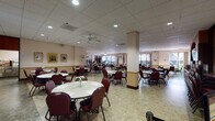 Located at 1530 Fifth Street in Santa Monica, California, this single-floor community facility is designed to accommodate group dining, gatherings, and events. The main hall is expansive and open, featuring drop-tile ceilings with recessed lighting and ceiling fans that create a bright, well-ventilated atmosphere. Numerous round tables with cushioned burgundy chairs are arranged throughout the space, providing flexible seating for large groups. Large windows along the perimeter allow natural light to fill the room and offer views of the surrounding outdoor greenery.

A dedicated buffet service line runs along one wall, equipped with warming trays and stanchions for organized guest flow. Adjacent to this area, dark wood cabinetry with ample counter space houses a microwave and a mounted flat-screen television, providing functional utility for events. Decorative framed artwork and wall hangings add warmth and character throughout.

A quieter auxiliary dining room connects to a lush outdoor patio area, offering an intimate setting with garden views through floor-to-ceiling windows. This room features cheerful wall décor and additional round tables. The overall ambiance throughout the facility is welcoming and community-oriented, thoughtfully designed to support social engagement and shared dining experiences.