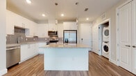 This well-appointed single-story residence in Myakka City, Florida, showcases a contemporary design with clean lines and a neutral color palette throughout. At the heart of the home is an open-concept kitchen that serves as a functional centerpiece, featuring a large granite-topped island, crisp white cabinetry, a gray tile backsplash, and a full suite of stainless steel appliances including a refrigerator with ice maker, range, and over-the-range microwave. Elegant pendant lights hang above the island, adding a modern touch. A convenient in-unit stacked washer and dryer is tucked neatly nearby. Wood-look plank flooring runs seamlessly throughout the entire home, providing both durability and warmth. The living area is bright and open, benefiting from natural light streaming through large windows and a glass-panel exterior door. The bedrooms are generously sized, each with ceiling fans, neutral walls, and ample natural light from well-placed windows with views of the outdoors. The bathrooms are finished to a high standard, featuring granite-topped white vanities, large mirrors, and white subway tile surrounds in the tub and shower areas. The overall ambiance is modern, clean, and move-in ready.
