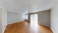 Located at 8926 N Lamar Blvd in Austin, TX, this single-floor unit offers an efficient and functional layout designed to maximize every square foot. The living room serves as the heart of the space, featuring warm wood-look laminate flooring that extends throughout the unit and neutral gray walls that create a clean, versatile backdrop. Natural light filters in through a side window and a sliding glass door dressed with vertical blinds, which also provides outdoor access. The textured popcorn ceiling adds a classic residential character to the space. A pass-through window connects the living area to the kitchen, which is equipped with warm wood-toned cabinetry and black appliances, offering a practical and open feel between the two areas. A hallway leads from the living space to the bathroom and closet, providing a logical flow throughout the unit. The bathroom includes a full soaking tub with a tiled shower surround, chrome fixtures, and a toilet, all finished in crisp white tones. A dedicated closet offers convenient storage. The overall ambiance is bright, clean, and straightforward, making this Austin unit a practical option for those seeking a compact yet complete living space.
