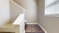 This 2-bedroom, 2-bathroom home offers a functional and cohesive layout finished in warm neutral tones throughout. The entrance welcomes you with dark hardwood-style flooring, a bright window with slatted blinds, and a white-paneled front door, setting a clean and consistent aesthetic carried through the home. A staircase with white-painted railings and matching dark wood treads adds architectural character near the entry.

The open-concept kitchen and living area serves as the heart of the home. The kitchen features rich dark cabinetry, a tile backsplash, stainless steel appliances, and a striking curved breakfast bar topped with granite countertops, illuminated by a modern drum pendant light. Crown molding adds a refined touch to the space.

Both bedrooms are carpeted in a neutral tone and include windows that allow natural light to filter in. The primary bedroom is generously sized and includes a ceiling fan with light fixture. Each bedroom is served by a closet for practical storage.

The bathrooms are finished with dark vanity cabinetry, granite countertops, and dark wood-style flooring, with a tiled tub-shower combo offering clean, classic styling. A dedicated in-unit laundry room accommodates a full-size washer and dryer with additional overhead shelving for storage convenience.