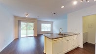 This single-floor, 1-bedroom, 1-bathroom residence offers a thoughtfully designed open-concept layout that seamlessly connects the kitchen and living areas. Rich, dark hardwood-style flooring runs throughout the main living spaces, creating a warm and cohesive aesthetic. The kitchen is appointed with white cabinetry, granite-style countertops, a center island featuring a stainless steel sink with a gold-tone faucet, and white appliances including a gas range and full-size refrigerator. The living area is bright and airy, benefiting from multiple windows and a sliding glass door that opens to an outdoor view of lush greenery, allowing ample natural light to fill the space. Track lighting adds a modern touch to the living and kitchen areas. The bedroom is carpeted for comfort and features a large window with outdoor views, as well as access to a generously sized walk-in closet outfitted with wire shelving on multiple levels. The full bathroom includes a white vanity with storage, a tub-shower combination with classic tile detailing featuring navy accent tiles, and hardwood-style flooring. A dedicated in-unit laundry area houses a full-size washer and dryer with overhead shelving, providing everyday convenience.