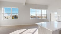 This thoughtfully designed single-floor space combines modern aesthetics with functional living. The open-concept living and dining area is bathed in natural light, courtesy of an array of large gridded windows that frame picturesque views of the surrounding landscape, including rolling hills and autumn foliage. Light-toned hardwood flooring flows seamlessly throughout, complementing the bright, neutral color palette that defines every room.

The kitchen is a standout feature, showcasing a contemporary design with two-tone cabinetry — crisp white upper cabinets paired with warm wood-grain lower cabinets. A sleek white quartz island anchors the space, while stainless steel appliances, including a refrigerator, range, microwave, and dishwasher, provide a polished, professional finish. A marble-effect tile backsplash adds a refined touch.

The bedrooms offer generous proportions, high ceilings, and ample natural light streaming through large windows. One bedroom includes access to a dedicated closet space.

The bathroom is finished to a high standard, featuring large-format marble-patterned tiles on both the floor and walls surrounding the soaking tub. A separate glass-enclosed shower and a bright window further elevate the spa-like ambiance. Throughout the space, clean lines, elevated finishes, and an abundance of natural light create a cohesive, modern living environment.