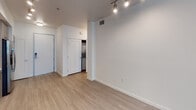 Located at 1105 E Katella Ave in Anaheim, California, this single-floor unit offers a clean, modern design throughout. The open-concept layout seamlessly connects the living area to the kitchen, creating a bright and functional space. Light wood-style flooring runs throughout the main living areas, contributing to the airy, contemporary feel of the unit.

The kitchen is well-appointed with two-tone cabinetry — white upper cabinets paired with warm wood-finish lower cabinets — complemented by a gray tile backsplash and light quartz-style countertops. A full suite of stainless steel appliances includes a gas range, over-the-range microwave, dishwasher, and a French door refrigerator with an ice and water dispenser. Track lighting overhead adds both style and practical illumination to the cooking and living space.

The bedroom is a comfortable, carpeted room with a window that allows natural light to filter in through blinds. The full bathroom features a tiled shower/tub combination, a modern floating vanity with a white countertop, a large mirror, and built-in open shelving for storage. Wood-look tile flooring ties the bathroom's aesthetic to the rest of the unit.

A dedicated laundry area with a stacked washer and dryer unit adds everyday convenience. The entry hallway provides a smooth transition into the living space, completing this thoughtfully designed Anaheim residence.