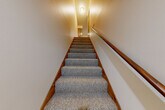 Located in Saginaw, Michigan, this 2-bedroom, 1-bathroom home offers a practical and well-organized single-floor layout with comfortable living spaces throughout. The combined dining room and kitchen is a functional highlight, featuring warm oak cabinetry, light countertops, a built-in desk area, and a classic chandelier overhead. Appliances include a range, refrigerator, and dishwasher, all set against carpeted flooring that continues throughout the home. The living room provides a generously sized, open area with textured ceilings and neutral tones, creating a welcoming atmosphere. The primary bedroom is a spacious retreat with large windows offering views of mature trees, filling the room with natural light. The second bedroom is cozy and well-lit, also featuring carpet and textured ceilings. A full bathroom with a tub-shower combination, tile flooring, oak accents, and a vanity with mirror serves both bedrooms. The home includes a utility room for added convenience, a hallway connecting the main spaces, and an impressive five closets providing abundant storage. A carpeted staircase with warm wood railings and wall-mounted lighting leads to additional space below, rounding out this efficiently designed home.