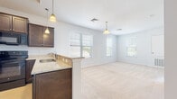 This well-designed single-floor residence offers a comfortable and functional layout with a clean, modern aesthetic. The heart of the home is an open-concept kitchen and living area, where rich dark-wood cabinetry pairs elegantly with light granite countertops. A peninsula with a stainless steel sink serves as a natural divider between the kitchen and the adjoining living space, while pendant lighting adds warmth overhead. Black appliances, including a range and built-in microwave, complete the kitchen's cohesive look. Light tile flooring anchors the kitchen area, transitioning seamlessly into plush, neutral-toned carpeting that extends throughout the living area and bedrooms. Multiple windows dressed with white blinds allow generous natural light to fill the open living space, creating an airy and inviting atmosphere. The bedrooms are generously proportioned with soft carpeting and ample natural light. The bathrooms feature dark wood vanities with wide countertops, large mirrors, tile flooring, and a dedicated walk-in shower with clean white surround. Throughout the home, neutral white walls and consistent finishes create a cohesive, move-in-ready environment that is both practical and comfortable.