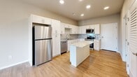 Located at 1735 E Valley Water Mill Rd in Springfield, MO, this one-bedroom, one-bathroom unit is thoughtfully designed to maximize functionality within a compact, single-floor layout. The open-concept kitchen and living area serves as the heart of the space, featuring warm wood-look flooring, recessed lighting, and a ceiling fan that enhances airflow throughout. The kitchen is well-appointed with crisp white shaker cabinetry, granite-style countertops, a center island with additional prep space, and a full suite of stainless steel appliances including a refrigerator, dishwasher, range, and microwave. A sliding glass door in the living area opens to a private balcony, bringing in natural light and outdoor views. The bedroom offers plush carpeting, a ceiling fan, and convenient access to both a walk-in closet and the adjacent bathroom. The bathroom continues the home's clean aesthetic with a white vanity and granite countertop. Additional practical spaces include a dedicated laundry area and utility room, rounding out this efficiently planned home with all the essentials for comfortable everyday living.