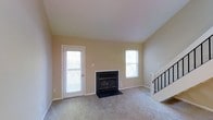 This two-story home offers a comfortable and functional layout designed to accommodate modern living. The main living area serves as the heart of the home, featuring soft, neutral-toned carpeting underfoot and warm beige walls that create a welcoming ambiance. A classic fireplace with a sleek black surround anchors the room, providing a focal point for relaxation and gathering. Large windows fitted with blinds allow generous amounts of natural light to filter through, brightening the space while offering privacy control. A glass-paneled exterior door provides convenient access to the outdoors and further enhances the sense of openness. A staircase with a black metal railing leads to the upper floor, adding a clean architectural detail that complements the home's overall aesthetic. The upper level extends the living space and provides additional versatility. Throughout the home, the neutral color palette and understated finishes create a blank canvas that is easy to personalize. The combination of natural light, plush flooring, and classic architectural elements makes this a warm and inviting space suited for a variety of lifestyles.