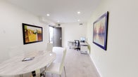 Located at 11525 Chandler Blvd in North Hollywood, Los Angeles, this single-floor commercial space offers a thoughtfully designed environment suited for professional use. The interior features a clean, modern aesthetic with light-toned walls, recessed lighting, and polished concrete flooring that transitions to carpet in the workstation area, lending a functional yet refined feel throughout.

A central meeting area anchors the space, furnished with a striking round marble-top table paired with sleek white chairs and a chrome pedestal base, providing an elegant setting for client meetings or collaborative sessions. A water dispenser nearby adds practical convenience. Large windows fitted with roller shades allow natural light to fill the room while offering privacy control.

The dedicated workspace features a contemporary L-shaped desk with built-in storage drawers, an ergonomic task chair, and a desktop monitor setup, creating an efficient individual work environment. A private entry door with an electronic keypad lock ensures secure access directly from the exterior.

Curated framed artwork adorns the walls throughout, including bold colorful prints and a standout landscape painting, adding visual character and warmth to the otherwise crisp, minimalist interior. The overall ambiance is professional and polished, making this space well-suited for a private office, consulting suite, or creative studio in the heart of Los Angeles.