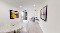 Located at 11525 Chandler Blvd in North Hollywood, Los Angeles, this single-floor commercial space offers a thoughtfully designed environment suited for professional use. The interior features a clean, modern aesthetic with light-toned walls, recessed lighting, and polished concrete flooring that transitions to carpet in the workstation area, lending a functional yet refined feel throughout.

A central meeting area anchors the space, furnished with a striking round marble-top table paired with sleek white chairs and a chrome pedestal base, providing an elegant setting for client meetings or collaborative sessions. A water dispenser nearby adds practical convenience. Large windows fitted with roller shades allow natural light to fill the room while offering privacy control.

The dedicated workspace features a contemporary L-shaped desk with built-in storage drawers, an ergonomic task chair, and a desktop monitor setup, creating an efficient individual work environment. A private entry door with an electronic keypad lock ensures secure access directly from the exterior.

Curated framed artwork adorns the walls throughout, including bold colorful prints and a standout landscape painting, adding visual character and warmth to the otherwise crisp, minimalist interior. The overall ambiance is professional and polished, making this space well-suited for a private office, consulting suite, or creative studio in the heart of Los Angeles.