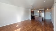 Located at 3303–3321 204th St SW in Lynnwood, Washington, this ground-floor unit offers a well-designed, single-level layout with a cohesive contemporary aesthetic throughout. Rich hardwood-style flooring runs continuously through the living, dining, and kitchen areas, creating a warm and unified feel across the open-plan space.

The kitchen is a standout feature, finished with deep espresso-toned cabinetry, a subway tile backsplash, quartz countertops, and a full suite of stainless steel appliances including an electric range, built-in microwave, and dishwasher. A peninsula with pendant lighting above provides additional counter space and a natural separation between the kitchen and the expansive living area.

The living area is generously proportioned and filled with natural light from large windows dressed with horizontal blinds, offering views of surrounding greenery. The neutral gray wall tones complement the warm flooring and create a calm, versatile backdrop.

The bathroom is clean and functional, featuring wood-style flooring that carries through from the rest of the unit, a full soaking tub with shower, and a bright, all-white finish. The overall design of the unit is modern and move-in ready, with thoughtful finishes that balance practicality and style throughout every room.