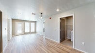 This single-floor unit in Rapid City, South Dakota, offers a clean, contemporary design with a neutral color palette and durable light-toned luxury vinyl plank flooring throughout the main living areas. The open living space is bright and welcoming, featuring a pendant light fixture and double French doors that invite natural light into the room. A dedicated in-unit laundry closet is conveniently accessible from the main living area, equipped with a full-size washer and dryer alongside built-in shelving. The kitchen is thoughtfully designed in an L-shaped layout with gray shaker-style cabinetry, white countertops, and a suite of black appliances including a refrigerator, dishwasher, electric range, and over-the-range microwave. A double-basin stainless steel sink completes the functional workspace. The bedroom features plush wall-to-wall carpeting, neutral-toned walls, and a window that brings in natural light. Two bathrooms serve the unit — one with a walk-in shower and one with a tub-shower combination — both finished with tile flooring and clean white fixtures. The overall layout is practical and well-proportioned, offering a comfortable and move-in ready living environment.