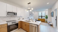 Located at 23 West Girard Avenue in Philadelphia, PA, this thoughtfully designed one-bedroom, one-bathroom residence offers a well-appointed layout across a single floor. The open-concept kitchen and living area forms the heart of the unit, anchored by a sleek peninsula with a white quartz countertop and seating for three. The kitchen is outfitted with stainless steel GE appliances, a marble-look tile backsplash, two-tone cabinetry combining white upper cabinets with warm wood lower cabinets, and a matte black faucet. An eye-catching multi-globe pendant light in brass and black adds a modern design accent overhead. The living area benefits from large floor-to-ceiling windows that flood the space with natural light and frame views of the surrounding Philadelphia streetscape. Light wood-toned flooring runs throughout, lending warmth and continuity to the space. The bedroom is a comfortable retreat, featuring a large window with city views and direct access to a closet. The full bathroom is finished with large-format stone-look tiles, a sliding glass-door walk-in shower with matte black fixtures, and a wood-toned vanity with a white countertop. Clean white walls and recessed lighting throughout create a bright, modern ambiance.