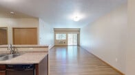 Located in Spokane, WA, this single-floor, 2-bedroom, 2-bathroom residence offers a well-organized and functional layout. The open-concept kitchen and living area serves as the heart of the home. The kitchen is outfitted with rich dark wood cabinetry, light countertops, black appliances including a refrigerator, range, microwave, and dishwasher, and a double-basin sink. Hardwood-style flooring flows throughout the kitchen and living areas, adding warmth and easy maintenance. The spacious living room features neutral walls, a wall-mounted air conditioning unit, and a sliding glass door leading to a private balcony with wooded views, complemented by an additional window that fills the space with natural light. Both bedrooms are carpeted and feature windows with outdoor views, warm neutral tones, and wood trim accents. The generously sized primary bedroom includes a walk-in closet with wire shelving for ample storage. The two bathrooms offer distinct configurations: one includes a sliding-door tub-shower enclosure, while the other features a full soaking tub, a dark wood vanity with a large mirror, and hardwood-style flooring. Overall, the residence presents a clean, comfortable ambiance with consistent finishes throughout.