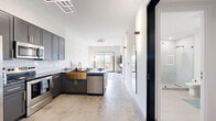 Located at 4750 Griffin Rd in Dania Beach, FL, this modern 2-bedroom, 1-bathroom residence offers a thoughtfully designed open-concept layout across a single floor. The combined kitchen and living area serves as the heart of the home, anchored by a striking kitchen that features charcoal grey shaker cabinetry with gold hardware, a bold brass farmhouse sink, dark marble-topped island with seating for four, white subway tile backsplash, and a full suite of stainless steel appliances. Polished concrete floors and geometric LED ceiling fixtures add a contemporary edge throughout. The living area is bright and airy, with large windows and a sliding glass door that opens to a private balcony overlooking lush greenery — an ideal spot for relaxing outdoors. The primary bedroom captures natural light through a large window with tree-lined views, while the second bedroom features a built-in Murphy bed with integrated grey cabinetry, maximizing versatility and storage. The bathroom is clean and spa-like, finished in large-format light tile with a frameless glass walk-in shower and matte black fixtures. A dedicated laundry area and closet provide practical storage solutions, completing this well-appointed Dania Beach residence.