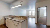 Located at 2500 Rimrock Rd in Madison, Wisconsin, this single-floor unit offers a well-designed, open-concept layout that balances modern finishes with functional living spaces. The kitchen is thoughtfully equipped with stainless steel appliances — including a range, over-the-range microwave, and refrigerator — complemented by dark, contemporary cabinetry, a green glass tile backsplash, and granite countertops that extend to a breakfast bar peninsula. White lower cabinetry with brushed hardware adds contrast and storage versatility. Hardwood-style flooring flows throughout the main living areas, creating a cohesive and easy-to-maintain surface. The living area is open and well-lit, with windows allowing natural light to fill the space. The bedroom features plush carpeting and includes access to a walk-in closet with wire shelving. A secondary room, also carpeted and naturally lit, offers flexibility for use as an additional bedroom or office. The bathroom is finished with dark tile flooring, a granite-topped vanity with white cabinetry, and a full shower-tub combination. Clean white walls, consistent trim details, and modern lighting fixtures throughout contribute to a cohesive, move-in ready aesthetic.