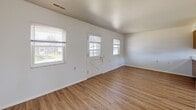 Located at 1450 Luther Square in Evansville, Indiana, this single-floor unit offers an efficiently organized layout comprising a combined kitchen and living area along with one full bathroom. The living area features light wood-style plank flooring and crisp white walls, creating a clean, neutral atmosphere. Multiple windows, including panels flanking a classic cross-brace entry door, allow natural light to fill the space and provide views of the surrounding neighborhood, contributing to an open and airy feel despite the compact footprint.

The kitchen is thoughtfully designed with warm honey-toned wood cabinetry spanning both upper and lower sections, providing ample storage. Light-colored countertops extend across the workspace, complemented by a peninsula that adds additional prep area and visually separates the kitchen from the living space. Essential appliances include a white electric range with overhead ventilation, a full-size refrigerator, and a stainless steel sink positioned beneath a window. The kitchen floor transitions to a neutral tile surface, adding a practical, easy-clean element.

The bathroom maintains a simple, functional design with tile-surround tub and shower, a window for natural light and ventilation, a single vanity with integrated sink, and tile flooring. Overall, the unit presents a straightforward, functional living environment.