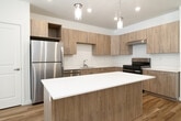 This thoughtfully designed 1-bedroom, 1-bathroom residence in Idaho Falls, Idaho offers a cohesive, modern aesthetic across its single-floor layout. The open-concept kitchen is a standout feature, boasting light wood cabinetry, stainless steel appliances, a white quartz countertop island with seating, and stylish pendant lighting — all set atop warm hardwood flooring. The kitchen flows seamlessly into the living room, which is bright and inviting, featuring recessed lighting, white walls, and French doors that open onto a private balcony, allowing natural light to fill the space. The bedroom is a comfortable retreat, finished with plush carpet, a large window dressed with classic checked curtains, and ample room for storage via a dedicated closet. The bathroom features a clean, minimalist design with a white quartz vanity, an undermount sink, modern fixtures, and a large mirror with overhead lighting. Throughout the residence, the consistent use of light tones, natural wood accents, and contemporary finishes creates a warm and cohesive ambiance well-suited for modern living.
