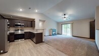 This single-floor residence showcases a thoughtfully designed open-concept layout where the kitchen and living area flow seamlessly together. The living space is anchored by vaulted ceilings with a ceiling fan, a fireplace with a dark-tiled surround, and plush carpeting that contrasts with the light wood-look flooring in the kitchen and entryway zones. Sliding glass doors lead to a private balcony, filling the living area with natural light and views of surrounding greenery.

The kitchen is well-appointed with dark espresso cabinetry, light granite-style countertops, and a full suite of stainless steel appliances, including a refrigerator, range, and over-the-range microwave. A peninsula provides additional prep space and serves as a natural divider between the kitchen and living areas.

The bedrooms are carpeted and include ceiling fans; at least one features a window with wooded views. Two bathrooms are finished with matching dark cabinetry, light countertops, and wood-look flooring. One bathroom includes a walk-in shower, while the other offers a more open layout. A dedicated laundry area houses a full-size Samsung washer and dryer, completing this functional and cohesive living space.