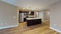 Located at 970 Center Rd in Buffalo, NY, this single-floor residence offers a thoughtfully designed layout with modern finishes throughout. The open-concept living and kitchen area serves as the heart of the home, featuring rich dark cabinetry, granite countertops, stainless steel appliances, and a large center island with an undermount sink illuminated by pendant lighting. Hardwood-style flooring extends through the main living areas, creating a warm and cohesive aesthetic. The living room is highlighted by a classic fireplace with a white mantel, a ceiling fan, and sliding glass doors that invite natural light and outdoor access. Bedrooms are carpeted for comfort and equipped with ceiling fans and windows that provide natural light. The primary bathroom features a granite-topped dark vanity, a walk-in glass shower, and wood-look flooring, while the secondary bathroom mirrors the same refined finishes with a full tub-shower combination. Neutral warm-toned walls throughout the space contribute to a welcoming and versatile ambiance, making this residence a comfortable and move-in ready home in the Buffalo area.