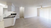 Located at 3605 Landings Way Dr in Tampa, Florida, this single-story residence offers a clean, functional layout designed for comfortable everyday living. The open-concept living and dining area is finished with light wood-look vinyl flooring and neutral walls, creating a bright, airy atmosphere. A pendant light fixture anchors the dining space, which also includes a utility closet. The kitchen is designed in a galley style, featuring white cabinetry with brushed nickel hardware, dark granite-style countertops, a stainless steel sink, white appliances including a range and refrigerator, and a tile backsplash. A pass-through counter connects the kitchen to the main living area, enhancing the open feel. The bedrooms are carpeted and offer ample natural light through vertical-blind-covered windows, with ceiling fans for climate comfort. Closet space is well-represented, including a walk-in closet with wire shelving in the primary bedroom. The bathrooms are finished with light wood-look flooring, white vanities, mirrors, and tub-shower combinations with tiled surrounds. Throughout the home, textured ceilings and crisp white trim provide a cohesive, well-maintained aesthetic.
