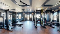 Located at 510 Cedar Tree Road in Wellford, SC, this fitness facility spans a generously sized single floor, thoughtfully divided into two dedicated exercise rooms connected by hallways. The main exercise room impresses with its coffered ceiling detail, ceiling fans, and recessed lighting set against deep navy-blue walls, creating a focused and energizing atmosphere. This room is comprehensively outfitted with a multi-station cable machine, a full rack system stocked with dumbbells, kettlebells, and weight plates, a rowing machine, adjustable benches, and full-length mirrors that enhance the sense of space. Treadmills are positioned near large windows, allowing natural light to pour in while offering outdoor views during cardio sessions. A second exercise room offers a distinct spin and functional training environment, featuring stationary cycling bikes with integrated screens, yoga mats, and stability balls. This room is bathed in natural light through expansive black-framed windows that overlook what appears to be a pool area, lending an open, airy feel. Decorative wall accents and a clean light-toned floor add a polished aesthetic touch. Together, the two rooms provide a well-rounded fitness experience suitable for strength training, cardio, cycling, and functional movement, all within a cohesive and professionally designed facility.
