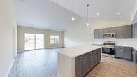 Located at 1810 NW Savannah Ln in Ankeny, Iowa, this well-appointed single-story home offers three bedrooms and two bathrooms within a thoughtfully designed floor plan. The open-concept kitchen and living area serves as the heart of the home, featuring striking gray shaker-style cabinetry, white subway tile backsplash, light quartz countertops, stainless steel appliances including a French door refrigerator and dishwasher, and a central island ideal for dining or entertaining. The living room impresses with soaring vaulted ceilings and a sliding glass door that floods the space with natural light and provides outdoor access. Durable light-toned hardwood-style flooring runs throughout the main living areas. The primary bedroom offers generous proportions, plush carpeting, multiple windows with neighborhood views, and a ceiling fan. It is complemented by a walk-in closet outfitted with wire shelving systems. The en suite primary bathroom features a glass-enclosed walk-in shower, white vanity cabinetry, and wood-look flooring. The second bathroom includes a full soaking tub with tiled surround. Additional bedrooms are carpeted and include closet storage. The attached garage provides ample parking and storage space, completing this modern, move-in-ready home.