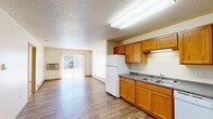 This single-floor unit offers a practical and functional layout designed for comfortable everyday living. The kitchen is a standout feature, equipped with abundant warm-toned wood cabinetry spanning both upper and lower sections, dark laminate countertops, and white appliances including a refrigerator, range, dishwasher, and microwave. A double-basin sink sits beneath under-cabinet lighting, and wood-look flooring ties the space together seamlessly.

The kitchen opens directly into a spacious living area, which benefits from natural light streaming through a sliding glass door fitted with vertical blinds. A wall-mounted air conditioning unit and baseboard heating provide year-round climate control. The living space offers a clean, open feel with neutral walls and the same durable flooring.

The bedroom features soft carpeting, a window allowing natural light, a baseboard heater, and a ceiling light fixture. An additional room with wood-look flooring and baseboard heating provides flexible use. The full bathroom includes a soaking tub, toilet, and wood-look flooring in a clean, neutral palette.

A dedicated in-unit laundry room houses a full-size washer and dryer with overhead wire shelving. The entryway features wood-tone doors, a closet, and direct access to a hallway leading to the bathroom and kitchen, providing an efficient and well-connected floor plan throughout.