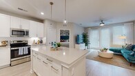 Located at 2989 Gulf to Bay Blvd in Clearwater, Florida, this single-floor residence offers a thoughtfully designed open-concept layout that seamlessly connects the kitchen, dining, and living areas. The kitchen is a standout feature, showcasing crisp white cabinetry extending to the ceiling, a large center island with a quartz countertop and bar seating, glass pendant lighting, and a full suite of stainless steel appliances. Light wood-style flooring runs throughout the main living areas, enhancing the bright, airy atmosphere.

The living room is anchored by floor-to-ceiling French doors that allow abundant natural light to fill the space, complemented by a ceiling fan overhead. The bedroom offers plush carpeting, a ceiling fan, and a generously sized walk-in closet with built-in wire shelving systems providing ample storage. A natural light source from a large window adds to the room's comfort.

The bathroom features a dual-sink vanity with white cabinetry, quartz countertops, framed mirrors, globe pendant lighting, and light wood-style flooring, delivering a clean, contemporary aesthetic throughout. The overall ambiance is modern, light-filled, and well-suited to Florida living.