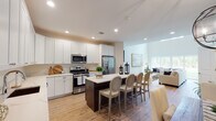 Located at 109 Comsewogue Rd in East Setauket, NY, this two-story villa at Villas At Setauket combines contemporary design with warm, inviting finishes throughout. The main level opens with a welcoming hallway finished in warm hardwood flooring that flows into the dining and living areas. The dining space features an elegant orb chandelier and is accented by large arched mirrors that amplify natural light. The open-concept kitchen is well-appointed with white shaker cabinetry extending to the ceiling, quartz countertops, stainless steel appliances, and a dark-toned center island with seating for several—seamlessly connecting to the living room beyond. The living area is bright and airy, with natural light streaming through large windows. An attached garage with an automatic opener provides convenient access and additional storage. Upstairs, the primary bedroom is a serene retreat featuring plush carpeting, ample closet space, and a luxurious en-suite bathroom with a glass-enclosed walk-in shower clad in full-slab marble-style tile. Additional bedrooms are carpeted, naturally lit, and include dedicated closets, making them equally suitable as guest rooms or a home office.