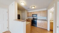 Located at 2015 W University St in Springfield, MO, this efficiently designed single-floor unit offers a well-organized layout comprising a living room, kitchen, bathroom, and two closets. The living room is bright and welcoming, featuring warm wood-look flooring, neutral walls, and a ceiling fan with light fixture. A large sliding glass door dressed with vertical blinds fills the space with natural light and provides outdoor access. The kitchen is thoughtfully appointed with light maple cabinetry, granite-style countertops, and a full suite of black appliances including a refrigerator, electric range with over-the-range microwave, and dishwasher. A peninsula counter adds additional workspace and a casual breakfast bar. The kitchen flows conveniently through the unit, with wood-look flooring continuing throughout. The bathroom features a vanity with a granite-style countertop and undermount sink, matching wood-look flooring, and clean, neutral finishes. Two closets provide practical storage solutions within the unit. The consistent use of warm flooring, neutral tones, and coordinated finishes throughout gives the space a cohesive and tidy aesthetic.
