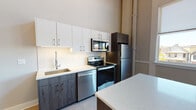 Located on Elmwood Avenue in Buffalo, NY, this two-floor residence showcases a contemporary design with high-end finishes throughout. The kitchen is a standout feature, outfitted with stainless steel appliances including a range, over-the-range microwave, dishwasher, and refrigerator. Two-tone cabinetry pairs crisp white upper cabinets with dark wood lower cabinets, complemented by quartz countertops, a textured tile backsplash, and an integrated sink. A kitchen island provides additional prep and dining space.

Soaring ceilings and large, multi-pane windows define the main living area, flooding the space with natural light and offering views of the surrounding neighborhood. The tile flooring on the main level transitions seamlessly between rooms, lending a clean, modern aesthetic.

The upper level features a railed loft-style overlook, accessible via a staircase, and includes well-appointed bathrooms. Each bathroom is finished with floating dark wood vanities, quartz countertops, backlit LED mirrors, and large-format tile flooring. One bathroom includes a glass-enclosed walk-in shower with full-height dark tile surround and a rain showerhead.

The lower level offers an additional versatile room with warm wood-look flooring, an architectural arched column detail, and a clerestory window that draws in natural light, making it a functional and inviting space.