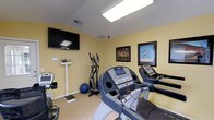 The fitness room at 100 Chapelridge Dr in Richland, Mississippi, is a dedicated single-floor exercise space designed to support an active lifestyle. The room features light yellow walls that create a clean, energizing atmosphere, complemented by a flush-mounted ceiling light panel that ensures consistent, even illumination throughout the space.

The room is equipped with multiple cardio machines, including treadmills and an elliptical trainer, providing a variety of workout options. A stability ball and a physician-style standing scale add to the functional fitness setup. A wall-mounted flat-screen television is positioned for easy viewing during workouts, enhancing the overall exercise experience.

Framed motivational sports prints decorate the walls, contributing to an encouraging and focused atmosphere. The neutral carpeted flooring provides a practical surface for the equipment arrangement. Ventilation is provided through ceiling vents, helping to maintain comfort during physical activity. Overall, this fitness room offers a compact yet well-appointed space with the essential amenities needed for effective daily exercise routines.