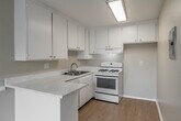 Located at 175 North Feldner Road in Orange, CA, this two-bedroom, two-bathroom unit offers a practical and well-organized single-level layout. The open-concept kitchen and dining area serves as a functional hub, featuring white cabinetry, speckled stone countertops, a gas range, and a built-in sink — all set atop warm light wood flooring. A peninsula counter provides additional workspace and a natural division between the kitchen and dining area. The spacious living room is bathed in natural light through large windows fitted with vertical blinds, and continues the light wood flooring for a cohesive feel. A wall-mounted AC unit provides climate control. Both bedrooms are carpeted in neutral tones and offer generous windows with outdoor views. The primary bedroom includes mirrored sliding closet doors that enhance the sense of space, while the second bedroom features direct access to a private balcony. Three closets throughout the unit provide ample storage. Both bathrooms are finished with speckled stone countertops and tub-shower combinations. Warm beige walls and white trim carry throughout, giving the entire space a clean, neutral, and move-in-ready aesthetic.