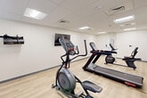 Located at 2712 Santa Maria Way in Santa Maria, CA, this fitness center offers a clean, functional space designed to support cardio-focused workouts. The room features light hardwood-style flooring that runs throughout, providing a bright and welcoming atmosphere underfoot. The drop ceiling with recessed panel lighting ensures consistent, even illumination across the entire space.

The fitness center is equipped with a well-rounded selection of cardio machines, including multiple treadmills, an elliptical trainer, a recumbent stationary bike, and an upright stationary bike. Additional fitness accessories, including exercise balls and free weights, are neatly organized along one wall, adding versatility to available workout options. A wall-mounted flat-screen television is positioned for easy viewing during exercise sessions.

The interior design is straightforward and utilitarian, with smooth white walls and gray baseboards that keep the focus on functionality. A keypad-secured entry door ensures controlled access to the facility. The layout is efficient, allowing comfortable use of all equipment without crowding. Overall, this fitness center provides a tidy, well-maintained environment suited for daily cardio and light exercise routines.