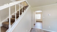 This three-floor home offers a thoughtfully designed layout with a blend of practical features and updated finishes throughout. The entryway greets visitors with a carpeted staircase framed by a classic white wood banister, leading to the upper level, with hardwood-style flooring flowing into adjacent rooms. Crown molding adds a refined architectural touch throughout the main living areas.

The kitchen is a standout space, featuring rich dark wood cabinetry, light stone-finish countertops, and a full suite of stainless steel appliances including a range, built-in microwave, and dishwasher. Light wood-style flooring ties the kitchen together with a clean, modern aesthetic.

The bedrooms are carpeted for comfort and finished with neutral tones. The primary bedroom is notably spacious, with dual windows that bring in generous natural light and a wide double-door closet providing ample storage. Additional bedrooms are well-proportioned and bright.

The bathroom is cleanly appointed with a dark wood vanity, light countertop, large mirror, wood-style flooring, and a window for natural ventilation and light.

The basement level offers a wide-open, unfinished space with a painted concrete floor and exposed ceiling joists, providing excellent potential for storage, a workshop, or future finishing. The electrical panel is conveniently accessible in this level.