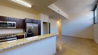 This single-floor unit blends industrial character with modern finishes, creating a distinctive living environment. The open layout is anchored by polished concrete floors that flow throughout the main living areas, complemented by painted white brick walls that lend an urban, loft-inspired aesthetic. A row of black-framed multi-pane windows lines the brick wall, allowing natural light to filter into the generous living space.

The kitchen is well-appointed with dark espresso cabinetry, light granite countertops, and a full suite of stainless steel appliances including a side-by-side refrigerator with ice maker, range, and built-in microwave. A peninsula with a granite top and integrated sink provides additional prep space and separates the kitchen from the living area.

Two bathrooms serve the unit, each featuring granite vanity tops, dark wood cabinetry, and undermount sinks. One bathroom includes a tub-shower combination, while the other, accented by exposed brick, offers a walk-in shower. A spacious closet with wire shelving provides ample storage, and carpeted bedroom areas offer a softer contrast to the concrete floors elsewhere. A bold dark entry door completes the industrial-modern character of the space.