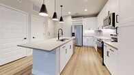 Located at 2908 East Howard Lane in Manor, TX, this modern single-story residence offers a well-designed 1-bedroom, 1-bathroom layout with a clean, contemporary aesthetic. Light-toned luxury vinyl plank flooring flows throughout the entire space, tying each room together cohesively.

The open-concept kitchen and living area serves as the heart of the home. The kitchen is outfitted with crisp white cabinetry, a subway tile backsplash, stainless steel appliances — including a refrigerator with ice maker, range, and over-the-range microwave — and a central island with a quartz countertop and undermount sink with a matte black faucet. A trio of pendant lights with black cone shades hang above the island, adding a modern accent. French doors with slatted blinds lead to an outdoor area, inviting natural light into the living space.

The bedroom is a comfortable, well-proportioned retreat featuring a ceiling fan, a window with exterior views, and direct access to the bathroom. The bathroom displays white cabinetry with a quartz-topped vanity, black hardware accents, and tile surrounds. Multiple closets provide generous storage throughout the unit.

The overall ambiance is bright, clean, and move-in ready, with a consistent modern design language carried through each space.