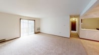 Parkland Green Unit 2 is a single-floor, two-bedroom, one-and-a-half-bathroom residence designed with a practical and straightforward layout. The living area is generously sized, featuring plush carpeting, a ceiling fan with integrated lighting, and baseboard heating. A built-in display cabinet adds a subtle decorative touch, while an open sightline connects the living space to the kitchen area.

The kitchen is well-equipped with dark wood cabinetry providing ample storage, light-toned countertops, tile flooring, and a full suite of white appliances including an electric range, refrigerator, and dishwasher. A breakfast bar separates the kitchen from the living area, and track lighting adds functional illumination. A range hood is installed above the stove for ventilation.

Both bedrooms are carpeted and feature ceiling fans with lighting fixtures, baseboard heating, and windows that allow natural light. Each bedroom includes closet access with dark wood-trimmed doors consistent throughout the unit.

The full bathroom includes a single-sink vanity with dark wood cabinetry, a large mirror, and a tub-shower combination. The half bathroom provides a toilet and sink, finished with tile flooring. Dark wood trim accents appear consistently throughout, giving the unit a cohesive, classic aesthetic.