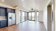 Located in Denver's vibrant LoHi neighborhood, this modern 3-bedroom, 2-bathroom residence offers a thoughtfully designed single-floor layout with contemporary finishes throughout. The open-concept living and kitchen area is bathed in natural light, courtesy of expansive floor-to-ceiling black-framed windows that frame sweeping city skyline views. Sliding glass doors provide direct access to a private balcony, while a ceiling fan adds comfort to the airy space. The kitchen is outfitted with navy blue cabinetry, stainless steel appliances including a range, dishwasher, and microwave, a white subway tile backsplash, and in-unit stacked washer and dryer. Wide-plank hardwood flooring runs throughout the main living areas, while the bedrooms feature plush carpet and ceiling fans. The primary bedroom benefits from large sliding glass doors opening to a balcony with striking downtown Denver views. Both bathrooms are finished with navy blue vanities, white quartz countertops, and matte black and gold hardware. The primary bath features a double-sink vanity, while the secondary bath offers a glass-enclosed shower. Additional storage is provided by closets in each bedroom, completing this well-appointed urban residence.