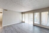 Located at 4001 Lakemont Dr in College Park, Georgia, this single-floor residence offers two bedrooms and two bathrooms within a well-organized layout. The spacious living room serves as the heart of the home, featuring durable wood-style flooring, textured ceilings, and white vertical-paneled accent walls. Large sliding glass doors and flanking windows flood the space with natural light and provide views of the outdoors, while vertical blinds offer privacy control. A bold black front door adds a distinctive architectural touch to the entry.

The kitchen is outfitted with white cabinetry, dark countertops, a black electric range with overhead ventilation, and matching wood-style flooring, providing a clean and functional cooking space. A hallway connects the main living areas to the private quarters.

Both bedrooms feature plush carpeting, neutral-toned walls, textured ceilings, and windows that bring in natural light. The generously sized primary bedroom includes a walk-in closet with built-in shelving and hanging rods on both sides, leading directly to a private bathroom. The bathrooms include a full bathtub and vanity with cabinet storage. The overall color palette of soft grays and whites creates a clean, neutral ambiance throughout the home.