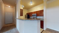 This single-story residence offers a well-organized layout with distinct living, kitchen, and bedroom areas, all finished with consistent, neutral-toned details throughout. The kitchen is a standout feature, equipped with rich cherry wood cabinetry, a tile backsplash, stainless steel appliances including a refrigerator, range, and microwave, and a granite-topped peninsula that separates the kitchen from the living area. Pendant lighting above the peninsula adds a decorative touch, while crown molding along the ceiling lends a refined character to the space. Light tile flooring runs through the kitchen, transitioning to plush carpet in the living room and bedrooms.

The living area is generously proportioned, featuring crown molding, a ceiling fan with light fixture, and a door with sidelight that invites natural light into the room. The bedrooms are carpeted and well-sized, each offering a calm, neutral palette and ceiling fans. The bathroom presents a elongated vanity with cherry wood cabinetry, a white countertop, a large mirror, tile flooring, and a full tub-shower combination with tiled surround. Overall, the residence provides a cohesive and functional living environment with classic finishing details throughout.