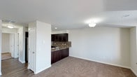 This single-floor unit offers one bedroom and one and a half bathrooms within a thoughtfully designed layout. The open living area features neutral carpet flooring and crisp white walls, creating a bright and clean atmosphere. A flush-mount light fixture illuminates the main living space, which flows seamlessly toward the kitchen area.

The kitchen is defined by rich, dark espresso cabinetry that provides ample storage, complemented by a stone-look countertop and a tile backsplash that adds texture and visual interest. A sink is positioned along the kitchen counter, which also functions as a subtle partition between the kitchen and living areas, enhancing the open-concept feel while maintaining a sense of definition between spaces.

Recessed lighting in the kitchen adds focused illumination, while the transition from carpet in the living area to hard flooring near the kitchen entry marks a practical material distinction. The overall palette — neutral walls, dark cabinetry, and warm-toned carpet — creates a cohesive, move-in-ready aesthetic suited for comfortable everyday living.