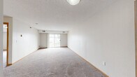 Located at 1119 41st St NW in Rochester, Minnesota, this single-floor, one-bedroom, one-bathroom unit offers a practical and efficient layout. The living room is a generous, open space featuring neutral carpet, a textured ceiling, and a sliding glass door that opens to a balcony, allowing natural light to fill the room and providing outdoor views. The kitchen is positioned adjacent to the living area and features oak cabinetry, a breakfast bar peninsula, tile flooring, and white appliances including a refrigerator and range with overhead ventilation. A functional layout connects the kitchen seamlessly to the rest of the unit. The bedroom is a well-proportioned, carpeted room with a window that brings in natural light and includes a full-width closet with bi-fold doors and wire shelving for organized storage. The bathroom is finished with large-format tile flooring, an oak vanity with a white countertop, and clean, neutral walls. Consistent wood baseboard trim throughout the unit ties the spaces together with a cohesive look. The overall ambiance is clean, understated, and move-in ready, offering a straightforward and comfortable living environment in a residential Rochester neighborhood.